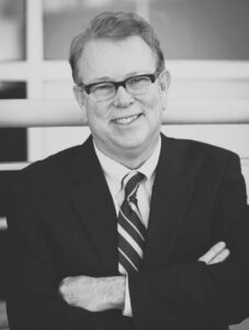 Brice Monighan: Lead Juror/AIA, NCARB in a suit smiling with arms crossed.